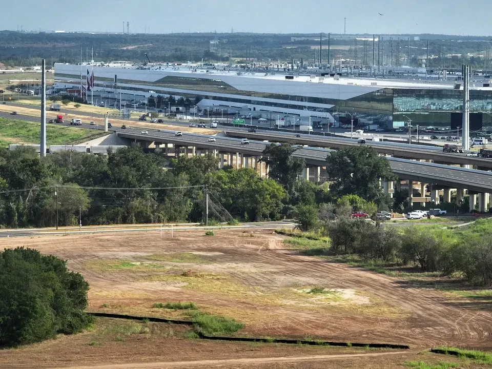 Aerial view of ground-clearing work at the Occam Foundry site in southeast Austin, with the highway and Gigafactory Texas beyond