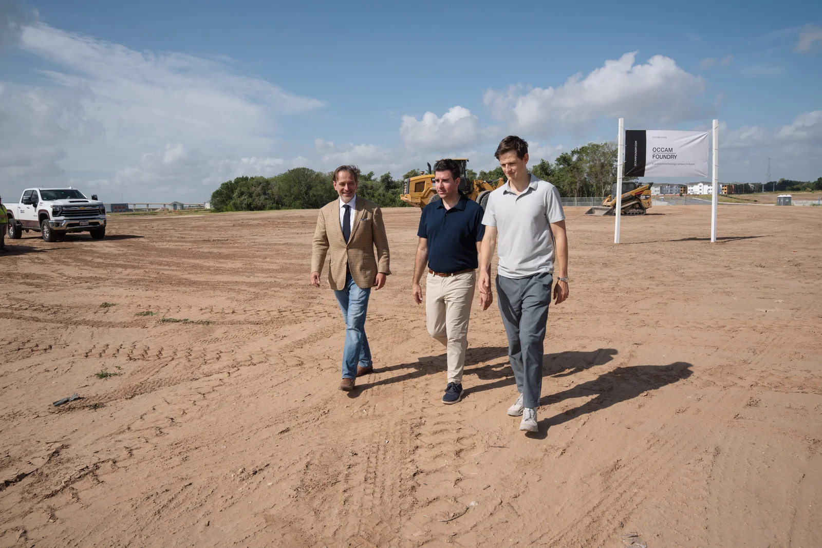 Three people walking the cleared site, equipment working behind them
